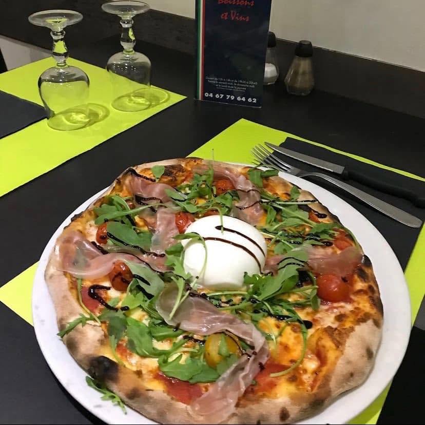 Une pizza cuite au feu de bois : jambon cru, roquette, tomates cerises et burrata, servie sur un set de table vert acide.