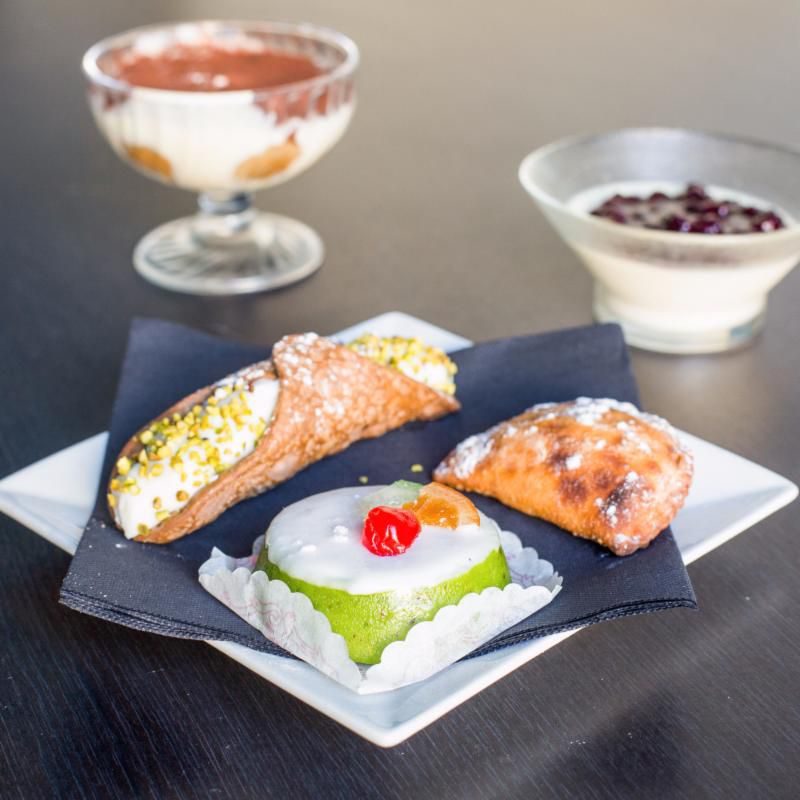 Assiette de pâtisseries siciliennes : cannolo aux pistaches, cassata au marzipan vert et une coupe crémeuse.