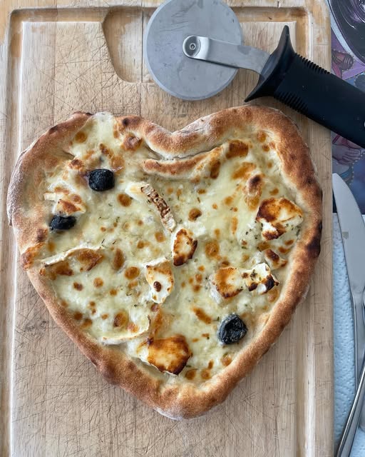 Pizza en forme de cœur sortie du four, posée sur une planche en bois.
